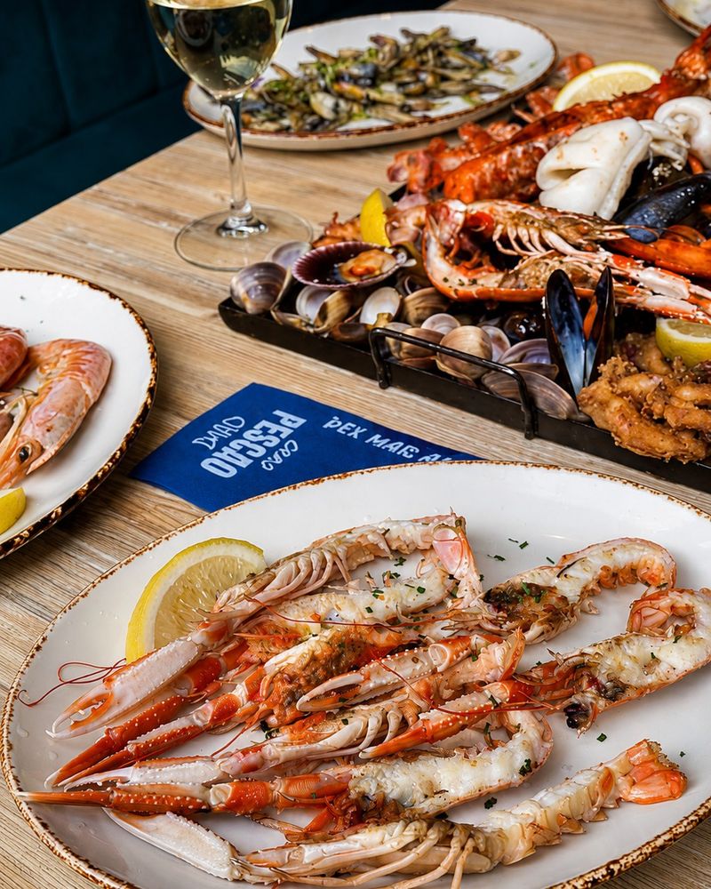 Cigalas a la plancha y bandeja de mariscada en una mesa de Chao Pescao con una copa de vino blanco