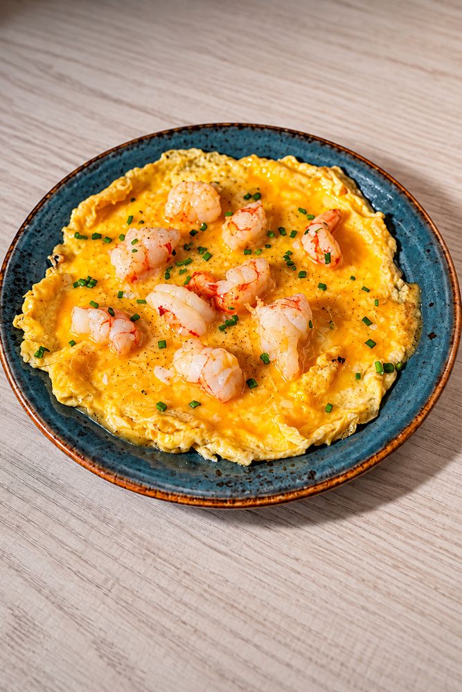 Tortilla abierta con gambas y cebollino servida en un plato azul de Chao Pescao